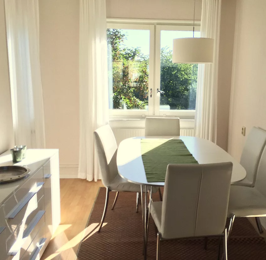 A picture of the dining area at Luzernvägen 10, with a table and chairs to the right, a sideboard to the left, and a window with curtains (photo).