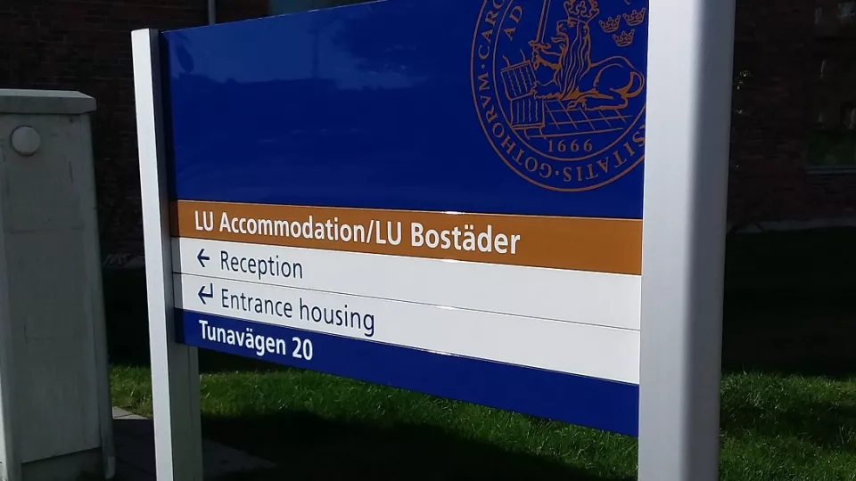 A blue brown and white sign that says LU Accommodation/LU Bostäder on the first row, Reception on the second row, entrance housing on the third row and Tunavägen 20 on the  forth row (picture)