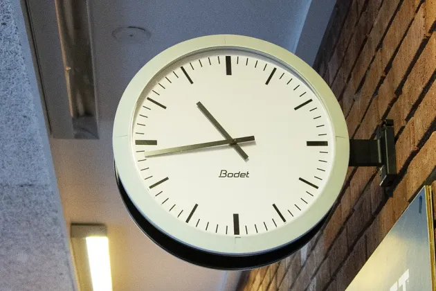 A large white analog clock suspended from a brick wall. Photo by Lund University