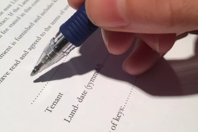 A hand holding a pen signing a paper contract. Photo by LU Accommodation.