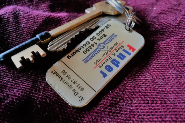 A close-up of a keychain with two keys and a keyfinder badge, on a purple background. Photo by LU Accommodation.