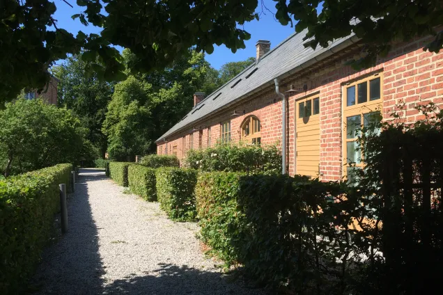 Annexet, a one and a half storey building with yellow wooden doors, and a gravel path lined with hedges. Photo by LU.