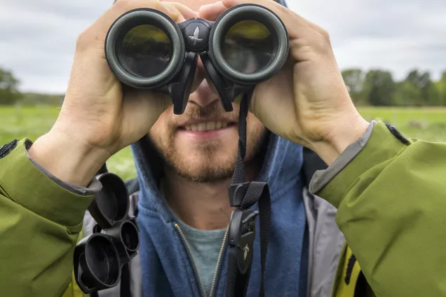 Picture of student looking through binoculars in a green field. Photo by Kennet Ruona.