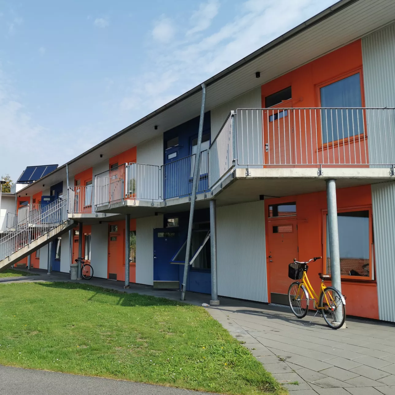 A white two-story building with a raised walkway, and doors painted alternating bright blue and orange. Photo by LU Accommodation.