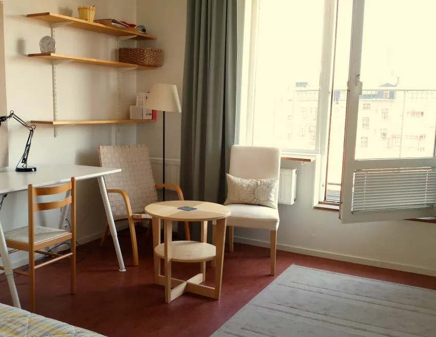 A picture inside a room at Spoletorp South, showing a desk, two chairs and a coffee table, and a french balcony (photo).