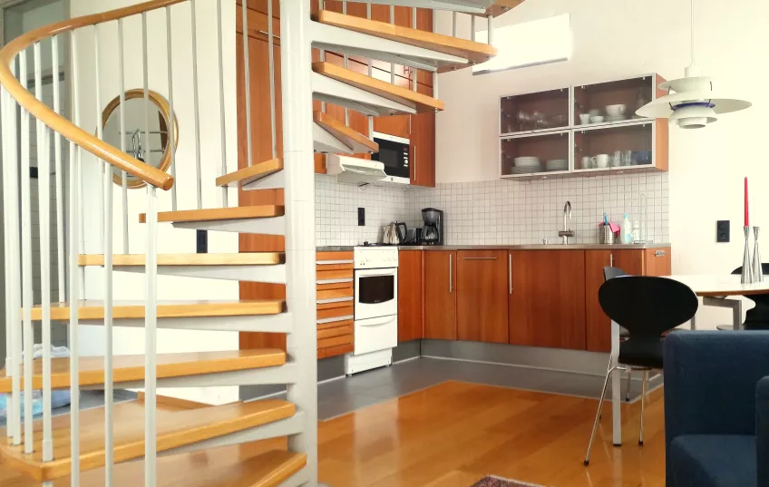 An overview of the combined living room and kitchen in apartment 5 at the housing area Biskopshusets annex showing the stairs to the second floor and the cooking area (picture)