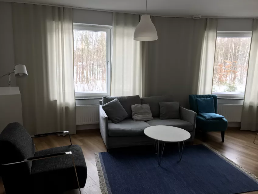 A living room at the housing area Bautastenen with a sofa, a small table, a rug, two armchairs, and windows with curtains. Photo by LU Accommodation.