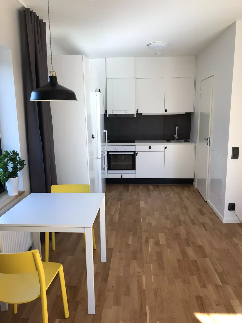 Overview of the kitchen in apartment 1201 at the housing area Albogatan showing the table and two chairs to the left and the kitchen area in the middle.