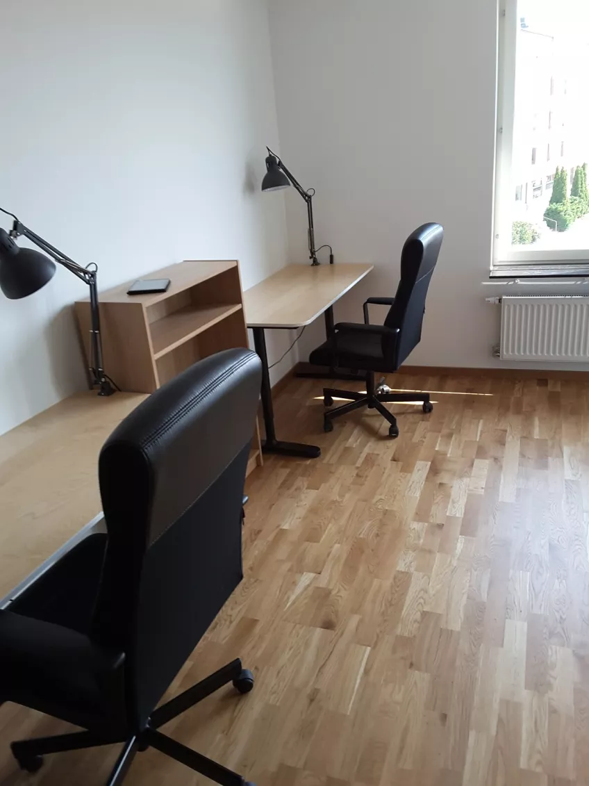 Overview of living room in apartment 1202 at housing area at Sofieberg showing two desk chairs, two desks with desk lamps and a small book case all to the left (picture)
