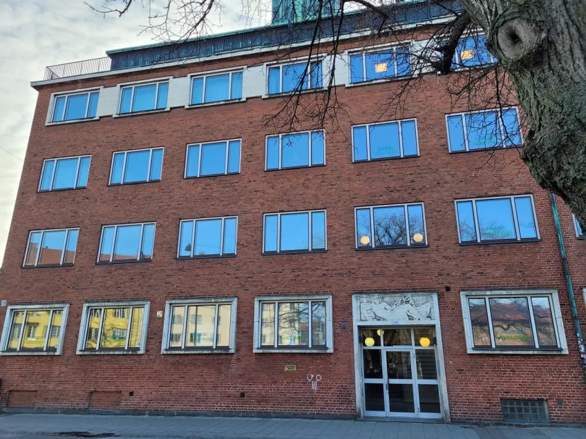 An overview of the housing area Folkets Park in the city of Malmö showing the building from the street. The building is in reddish brick and the windows of top three floors reflect the blue sky. (picture)