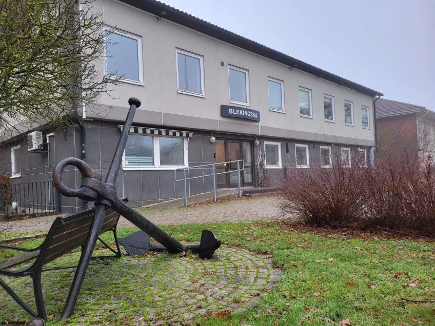 A two-story grey building with a large "Blekingska" sign, and an anchor sculpture in the foreground. Photo: Mikko Jokela Måsbäck