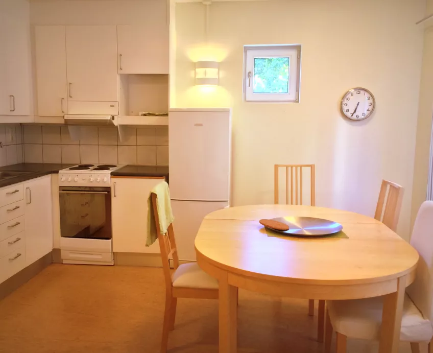 A kitchen area at Klostergården Student House with a dinner table, refrigerator, wall clock, and a stove and cabinets in the corner (